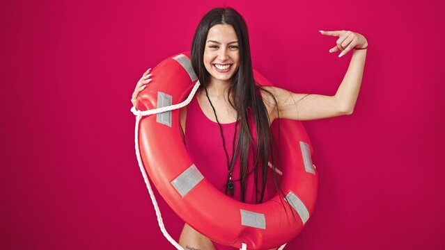 Young beautiful hispanic woman lifeguard holding lifeguard float pointing with finger over isolated red background