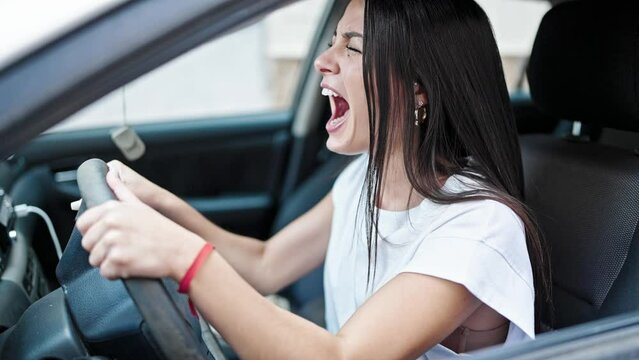 Young beautiful hispanic woman stressed driving car screaming at street