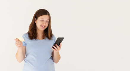 Online shopping. Portrait of smiling pregnant woman paying with plastic credit card on smartphone app, standing with mobile phone and bank card against white background