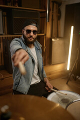 Stylish drummer in trendy outfit pointing drumstick to camera