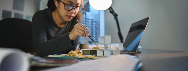 Architecture students diligently make house model building samples with paper architecture and tools at night in their alone room. Banner size with copy space.