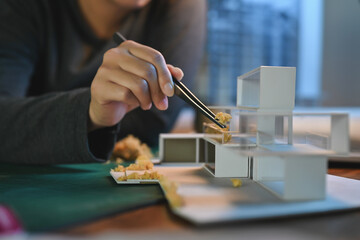 Close-up hand of Architect students diligently make house model building samples with paper art...