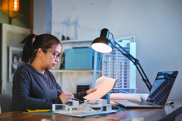 Architecture students diligently study the detail in blueprints and make house model building samples with architecture tools at night in their alone room.