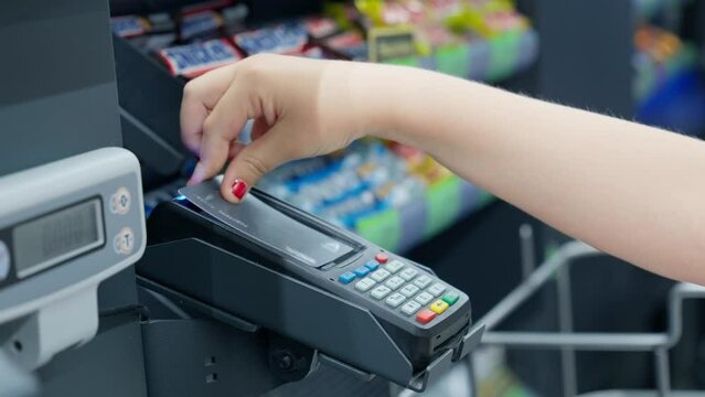 Customer little girl paying for purchases using credit card. Child hand with credit card in front of terminal. Payment by credit card in terminal. Close-up in 4K, UHD