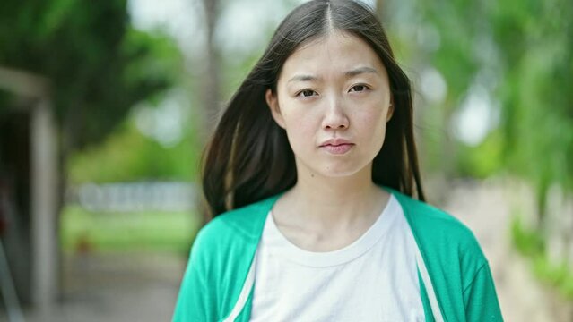 Young chinese woman standing with serious expression at park