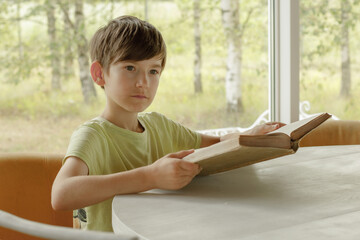 A child sits at the table and reads an old book. A boy with a book in his hand. A child's lesson...