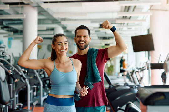 Happy athletic couple flexing their muscles after working out in gym and looking at camera.