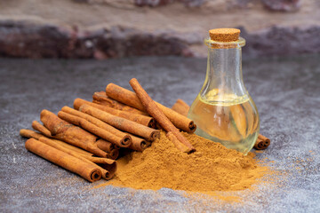 Essential cinnamon oil in a small bottle, ground cinnamon and cinnamon sticks on old wooden background, selective focus