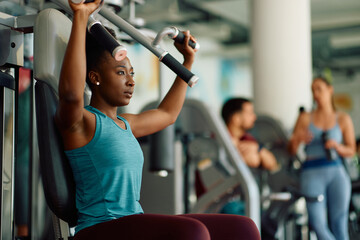 Fototapeta premium Yong black athletic woman doing weight exercises for upper body strength during sports training in gym.