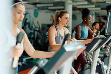 Group of athletes exercising on cross trainer while working out in gym.