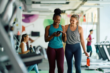 Happy athletic women using cell phone during sports training in gym.