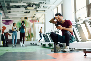 Fototapeta na wymiar Happy athlete using smart phone while taking break after exercising in gym.