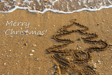 Merry Christmas from a tropical climate. Fir tree painted on the sand near the sea. Card