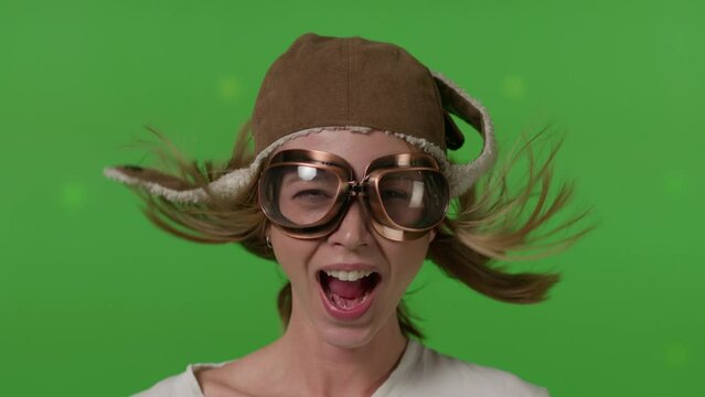 Close-up of a girl's face in a retro pilot's hat blown by a strong wind on Green screen background, chroma key.