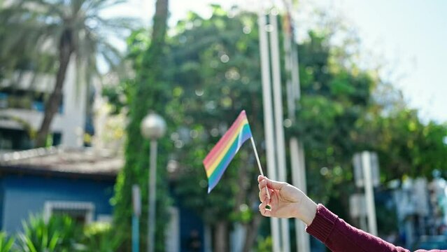 Young hispanic man holding rainbow flag at park