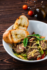 Meat salad with beef slices, sweet pepper, lettuce, greens and fried toasts in a plate.