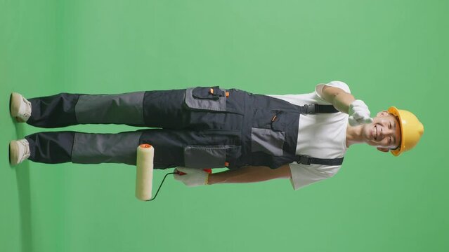 Full Body Of Asian Man Painter Wearing Safety Helmet Smiling And Touching His Chest Then Pointing At You While Standing In The Green Screen Background Studio
