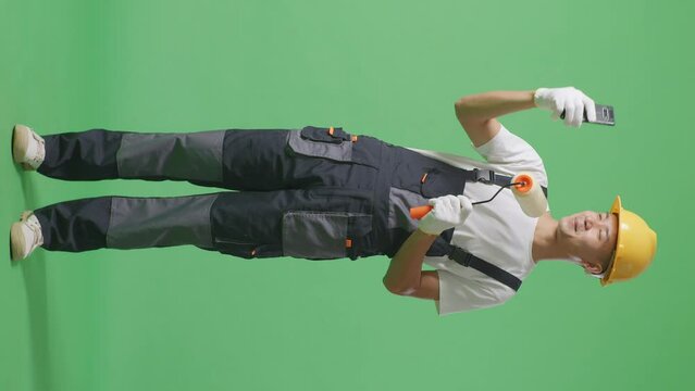 Full Body Of Asian Man Painter Wearing Safety Helmet Using Smartphone Taking Picture While Standing In The Green Screen Background Studio
