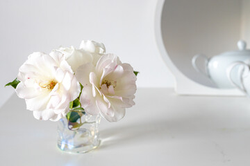Tea white rose in a transparent glass on white table. Place for text.