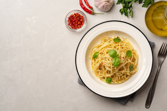 Spaghetti aglio e olio. Traditional Italian pasta with garlic, olive oil and chili peppers in plate on concrete background.