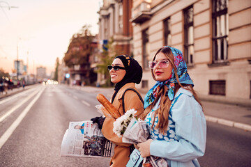 Couple woman one wearing a hijab and a modern yet traditional dress, and the other in a blue dress...
