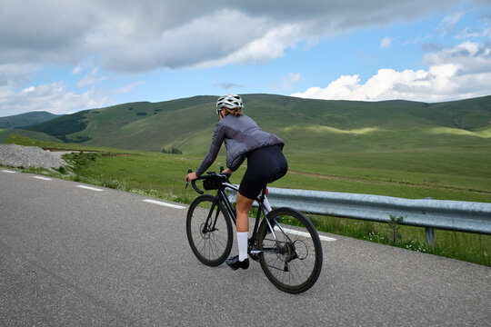 Fit female cyclist wearing cycling kit and helmet riding on the road on a gravel bike. Empty mountain road. Sports motivation image. Bucegi Mountains