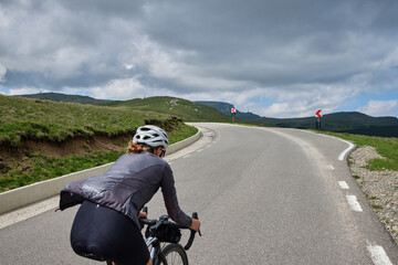 Woman cyclist riding a road bike with a view of the mountains. Sport motivation.Female cyclist wearing a cycling kit and helmet.Bucegi Mountains