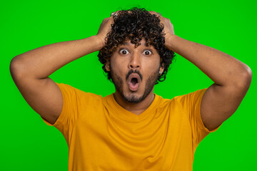 Oh my God, Wow. Excited amazed winner man raising hands in surprise looking at camera with big eyes shocked by sudden victory. Sincere handsome indian guy isolated alone on green chroma key background