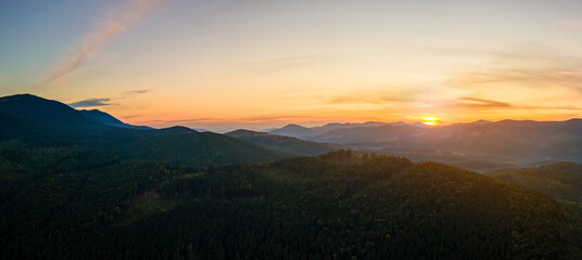 Aerial view of dark mountain hills with bright sunrays of setting sun at sunset. Hazy peaks and misty valleys in evening