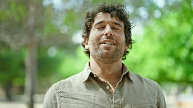 Young hispanic man smiling confident breathing at park