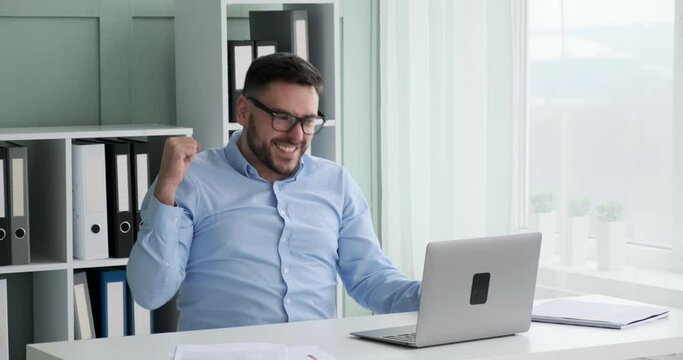 Caucasian businessman sitting at his desk in his office, working on his laptop. Suddenly sees something that makes him incredibly happy.