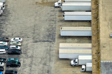 High angle view of big commercial shipping center with many freight trucks unloading and uploading goods for further distribution. Global economy concept