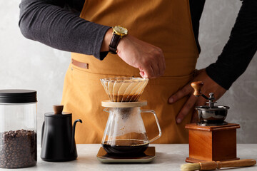 Artistic Male Barista Expertly Crafting Hot Pour-Over Coffee with Timely Precision, Surrounded by Coffee Maker and Accessories in Natural Light - White Background