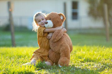 Pretty child girl tenderly embracing her teddy bear friend outdoors on green grass lawn. Concept of...