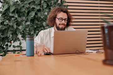 Smiling male freelancer working on laptop while sitting in modern coworking. Remote work concept