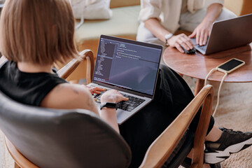 Back view of young woman programmer writes program code on laptop while sitting in modern coworking