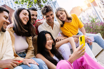 Young group of gen z people having fun using cell phone together outside. Cheerful community of...