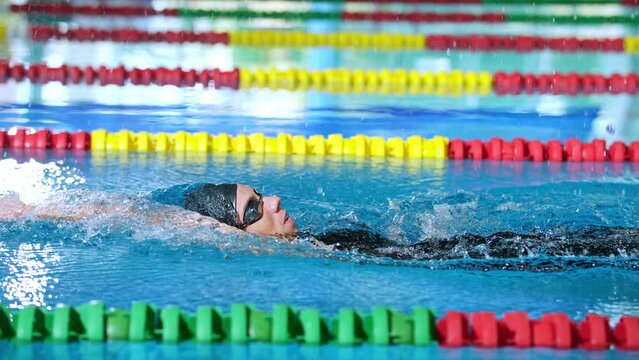 Female athlete in action, performing the backstroke swim technique in the indoor lap pool, tracking close up shot. Competitive back crawl stroke concept.