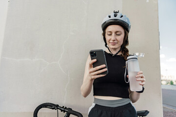 Uses a bicycle app, a young woman in a helmet training on a bicycle rides, uses a water bottle....