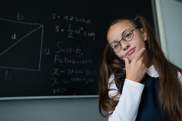 Caucasian schoolgirl in glasses answers at the blackboard pointing with a pointer.