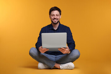 Happy man with laptop sitting on yellow background