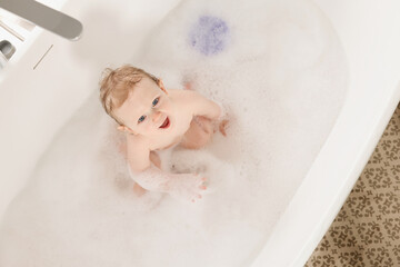 Cute little baby bathing in tub at home, top view