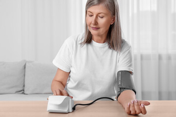 Woman measuring blood pressure at wooden table in room