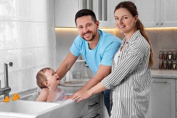 Fototapeta premium Father and mother washing their little baby in sink at home