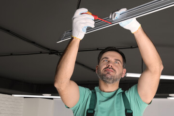 Ceiling light. Electrician installing led linear lamp indoors