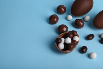 Tasty chocolate eggs and different sweets on light blue background, above view. Space for text