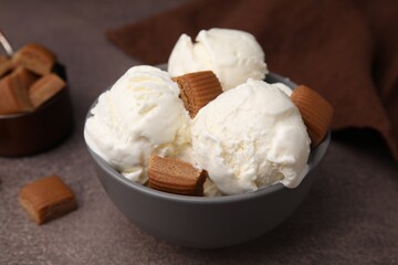 Scoops of ice cream with caramel candies in bowl on textured table, closeup
