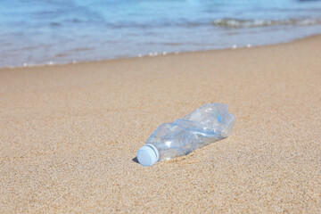 Used plastic bottle on sand near water. Recycling problem