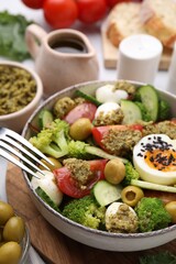 Delicious salad with pesto sauce in bowl and fork on table, closeup