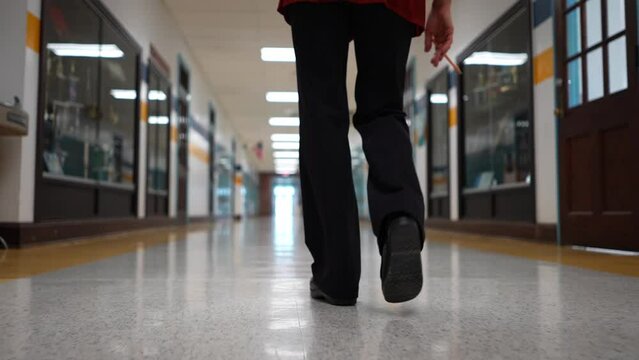 Low angle slow motion of teachers shoes walking down an empty school hallway with US flag in the distance.
